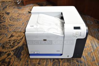HP Color LaserJet CP3525x printer in good condition, features control panel, model label, placed on patterned carpet.