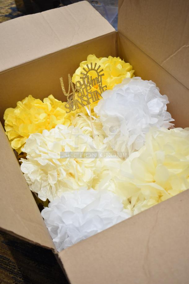 Cardboard box filled with yellow and white paper poofs and a gold glitter sign reading "You are my Sunshine."