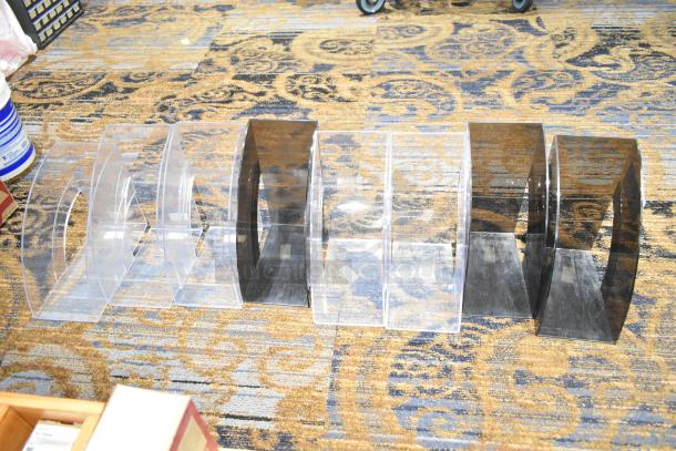 Eight plastic magazine organizers, clear and black, in good condition, displayed on patterned carpet.