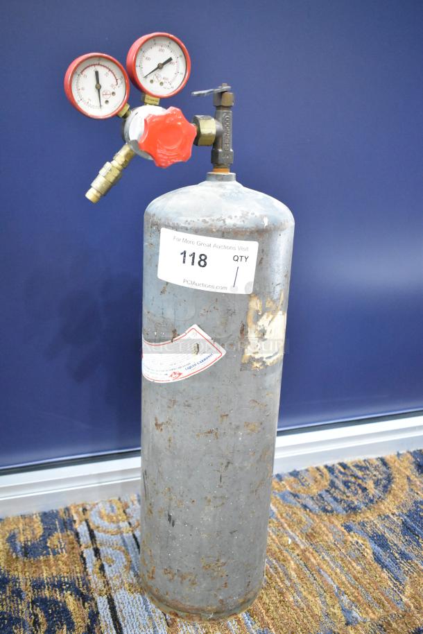 Acetylene tank with regulator and gauge, showing signs of wear. Labels include auction details and safety information. Buyer pick-up only.