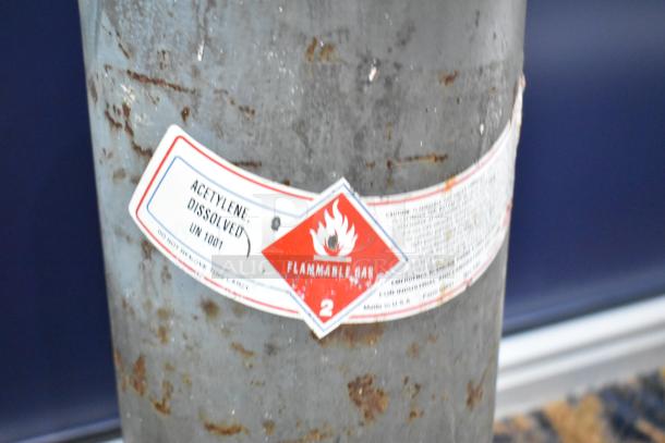 Acetylene tank with label "Acetylene, Dissolved UN1001" and "Flammable Gas" marking. Rusted surface, pick up only.