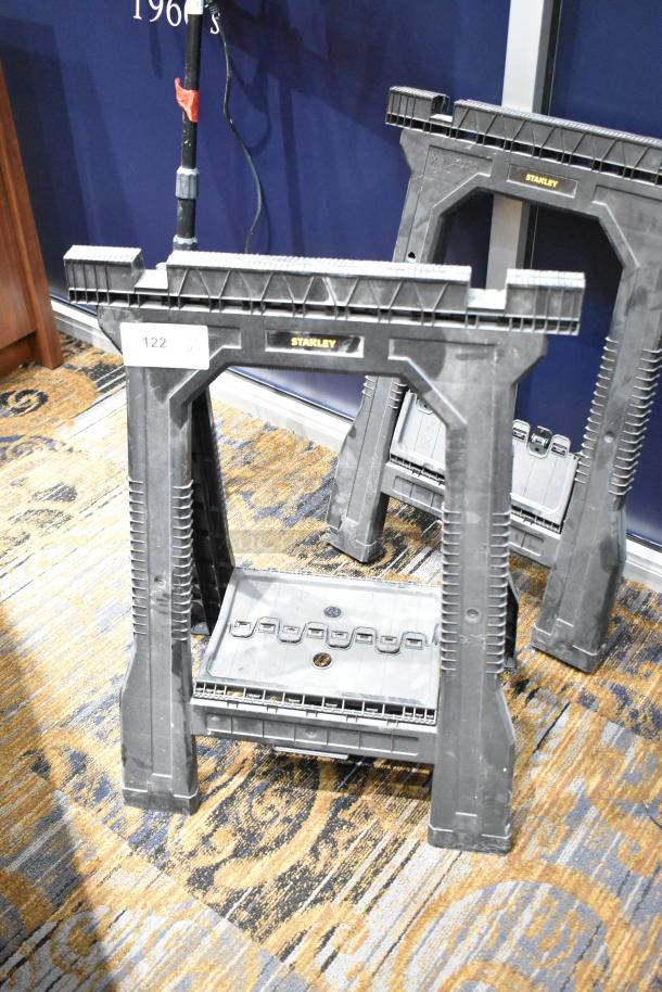 Two Stanley black poly sawhorses, sturdy design, visible brand label. Suitable for heavy-duty tasks.