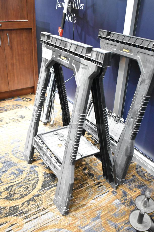 Two Stanley black poly sawhorses, durable plastic, stackable design, labeled with Stanley logo, in good condition.
