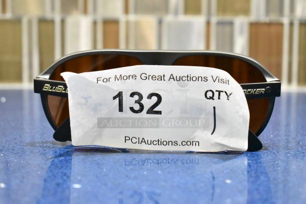 Brand new black framed sunglasses with BluBlocker brown lens, shown with auction tag number 132 on PCI Auctions.