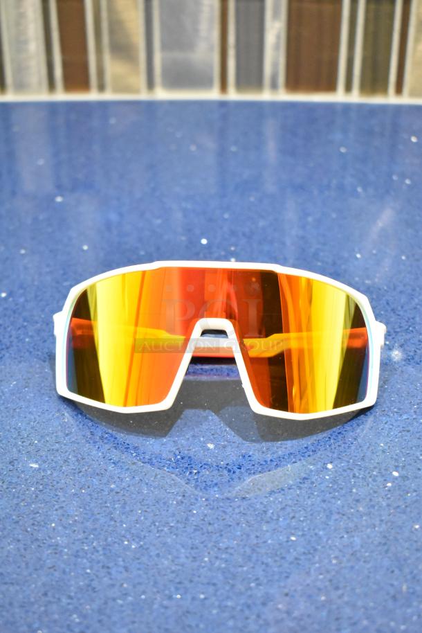 Brand new white-framed sunglasses with BluBlocker orange lenses, reflective surface, and geometric design.