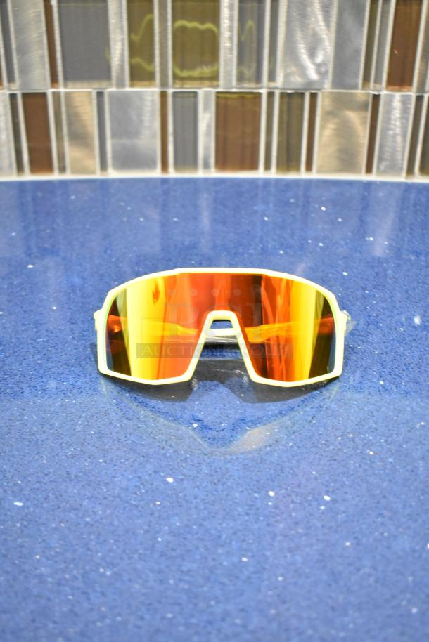Brand new white-framed sunglasses with BluBlocker orange lenses on a blue surface.