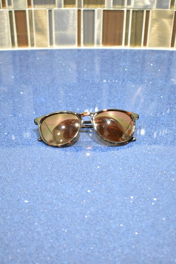 Brand new tortoise shell framed sunglasses with BluBlocker brown lenses, glossy finish, on a sparkly blue surface.
