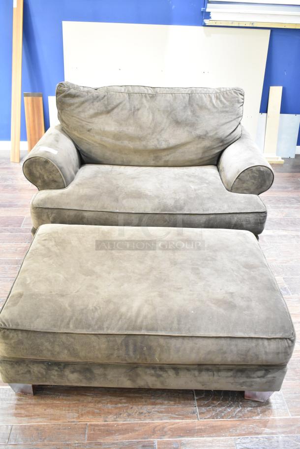 Gray arm chair with ottoman, plush fabric, slightly worn, rounded armrests, suitable for living room seating.