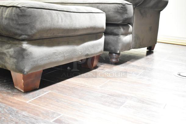 Gray arm chair with matching ottoman, wooden legs, upholstered in soft fabric, showing light wear, on wooden floor.