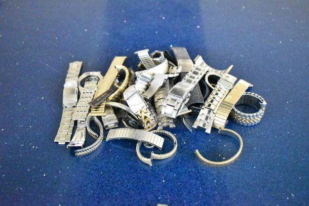 Assorted watches and metal watch bands in a pile on a blue surface, showcasing various styles and finishes.