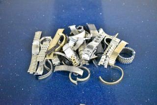 Assorted watches and metal watch bands in a pile on a blue surface, showcasing various styles and finishes.