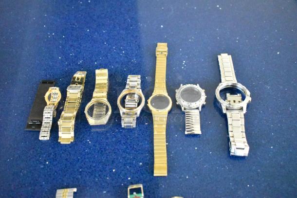 Lot of various watches and watch bands in assorted styles and materials on display, showing metal bracelets and empty watch cases.