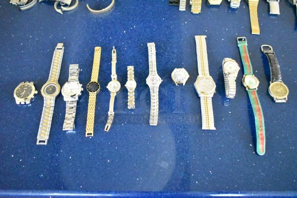 Lot of various watches and watch bands on a blue surface. Includes metal, leather, and fabric bands. Mixed conditions.