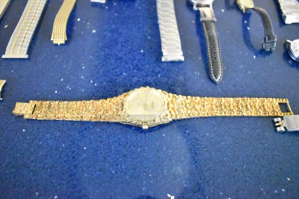 Five assorted watches with varied bands on display, including a gold-toned watch with textured band, laid out on a blue surface.