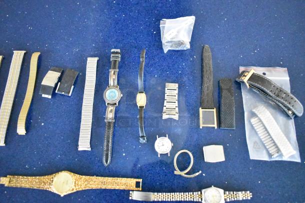27 assorted items including 5 watches and various watch bands, mixed materials, pre-owned, laid on blue surface.
