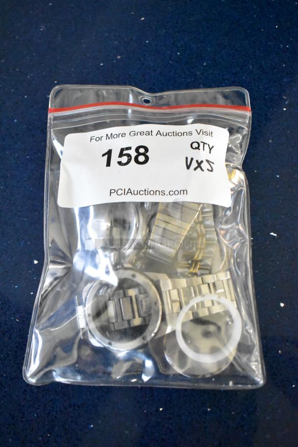 Sealed bag with four metallic watch cases and a watch band. Auction lot label 158, website link visible.