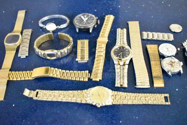 Assorted items including various watches and watch bands on a blue surface. Includes gold and silver tones, some branded like Citizen.