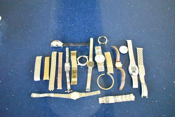 32 assorted watches and watch bands on a blue surface. Each item varies in style and condition, showcasing diverse options.