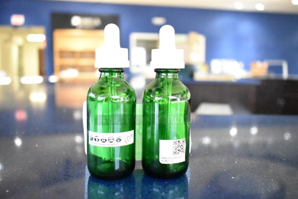 Two green glass dropper bottles with white caps. One bottle has a label with icons and "106," the other a QR code.