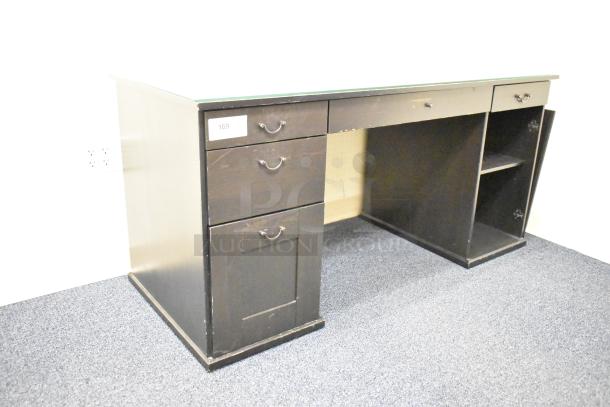 Wooden desk with five drawers, dark finish, metal handles, signs of use. Desk tag numbered 169. Suitable for office use.