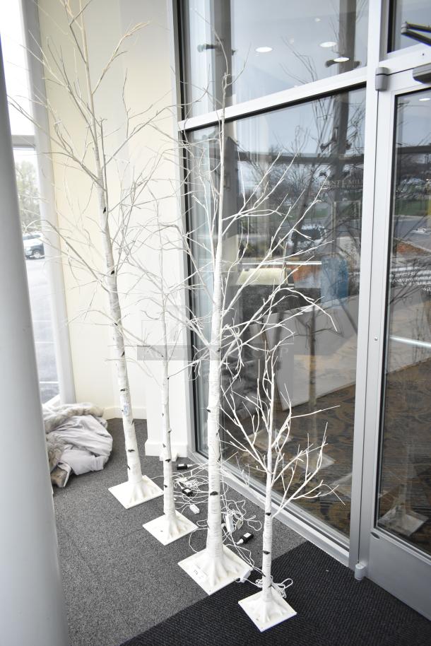 Four light-up fake trees with white branches, sturdy bases, and visible power cords, perfect for indoor decor.
