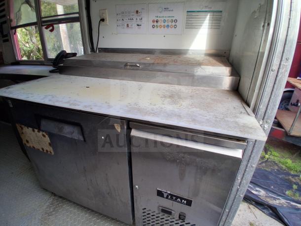 Food trailer interior with grease hood, stainless steel surfaces, Royal Range, Avantco griddle, Titan refrigeration unit displaying moderate wear.
