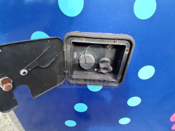 Food trailer charging port with open cover, showing electrical socket. Blue exterior with light blue polka dots.
