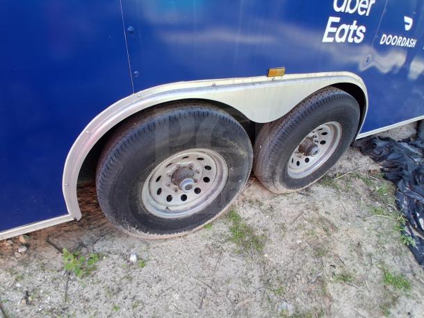 Food trailer with Uber Eats, DoorDash logos, dual wheels, and grease hood system, parked on dirt.