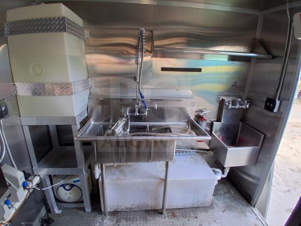 Commercial kitchen trailer interior with stainless steel double sink, high-arc faucet, and Arctic Air refrigeration. Features grease hood, Dean fryers, Sierra griddle, Wells 4-burner cooktop.