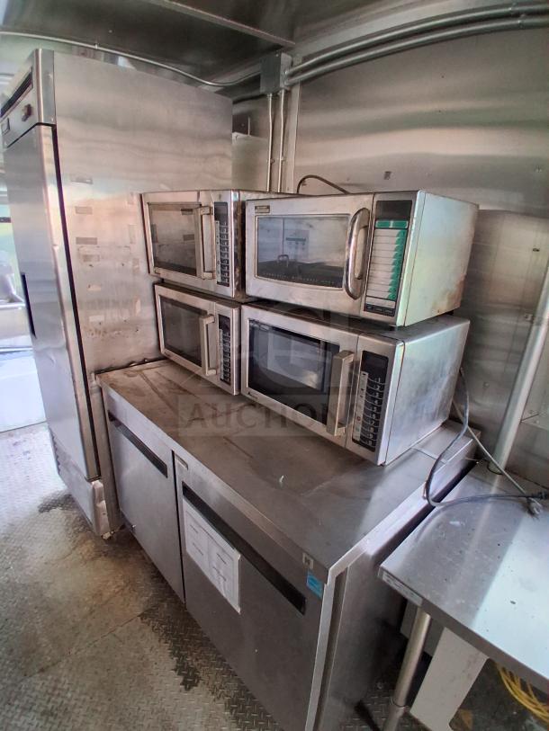 Commercial kitchen trailer interior with Arctic Air refrigeration suite, multiple microwaves, and stainless steel surfaces, used condition.
