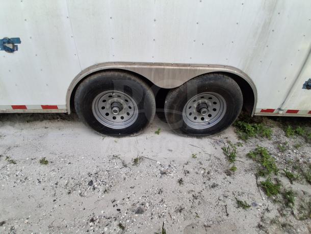 Commercial kitchen trailer with dual axle wheels, white exterior, visible wear, and secure blue latch on sandy ground.