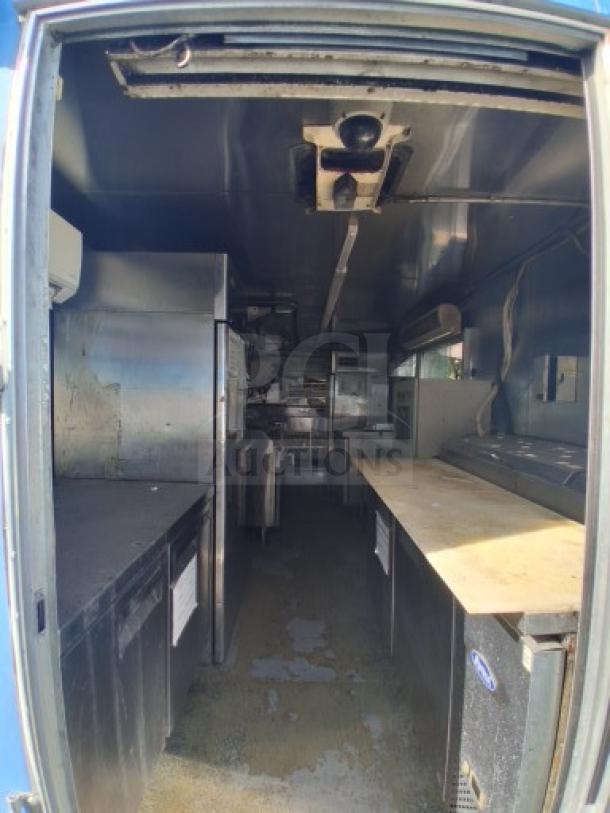 Commercial kitchen trailer with large order window, equipped with grease hood, dual fryers, griddle, burner cooktop, and complete refrigeration suite.