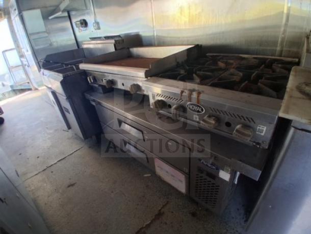 Commercial kitchen trailer interior featuring a Royal brand griddle, burner cooktop, dual fryers, grease hood, and refrigeration unit in good condition.