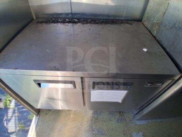 Commercial kitchen trailer refrigeration unit with dual drawers, visible surface wear, and installed at floor level.