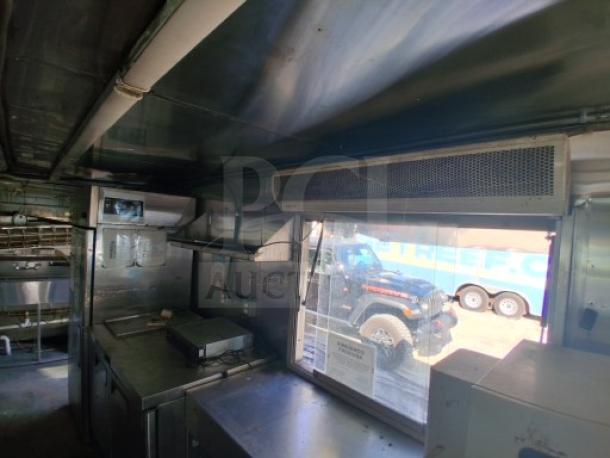 Commercial kitchen trailer with large order window, grease hood, dual fryers, griddle, burner cooktop, refrigeration suite.