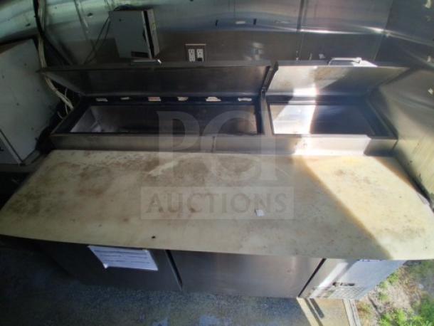 Commercial kitchen trailer interior with prep area, refrigeration suite, and open lids. Visible outlets and metal surfaces.