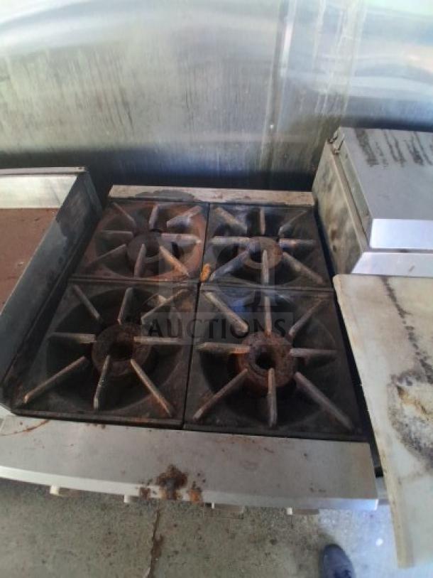 Commercial kitchen trailer interior showing a four-burner cooktop. Signs of use are visible around burners.