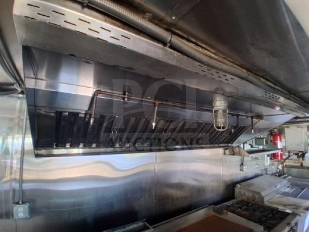 Commercial kitchen trailer interior with large grease hood, dual fryers, griddle, burner cooktop, and refrigeration suite.