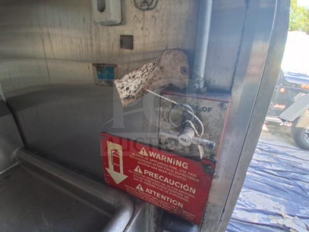 Commercial kitchen trailer interior with visible warning label and shutoff valve. Equipped for high-capacity cooking.