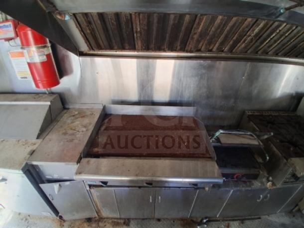 Food trailer interior with stainless steel commercial kitchen appliances, including a flat-top grill and fire suppression system. Signs of wear.