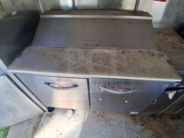 Commercial-grade stainless steel refrigeration unit inside a food trailer, showing signs of wear. Ideal for catering or street vending.