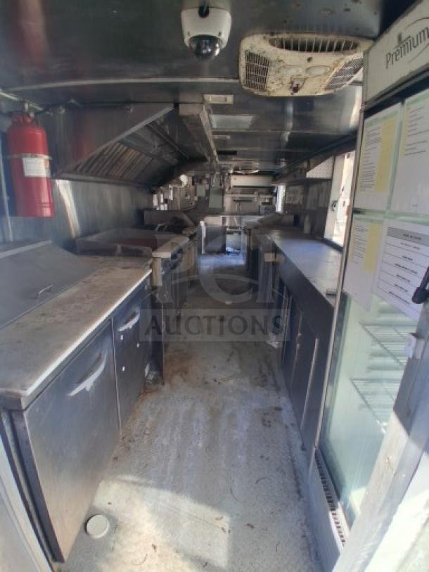 Food trailer interior with commercial kitchen equipment, including stoves, countertops, and fire extinguisher. Some wear visible.