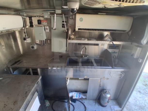 Fully equipped food trailer interior with stainless steel counters, triple sink, air conditioning unit, and utility connections.
