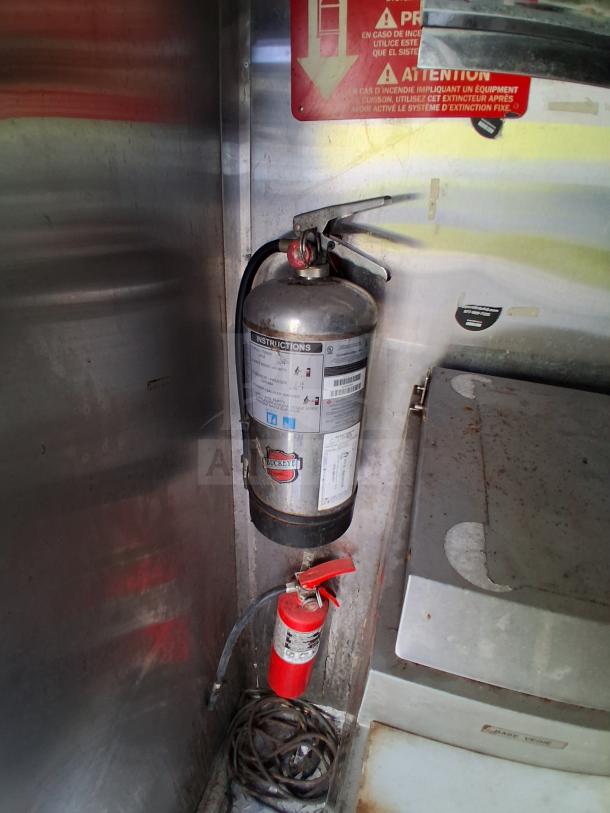 Mobile kitchen interior with Buckeye fire extinguisher, fire suppression system, and control panel. Stainless steel surfaces.