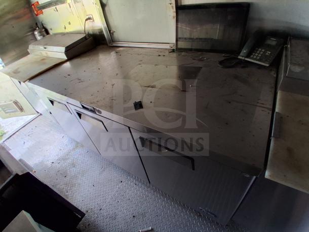 Mobile kitchen trailer interior with stainless steel countertops, commercial refrigeration, and fire suppression system.