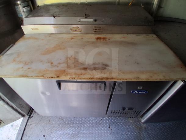 Mobile kitchen workstation with commercial refrigeration, stainless steel finish, and a used cutting board, featuring climate and fire controls.