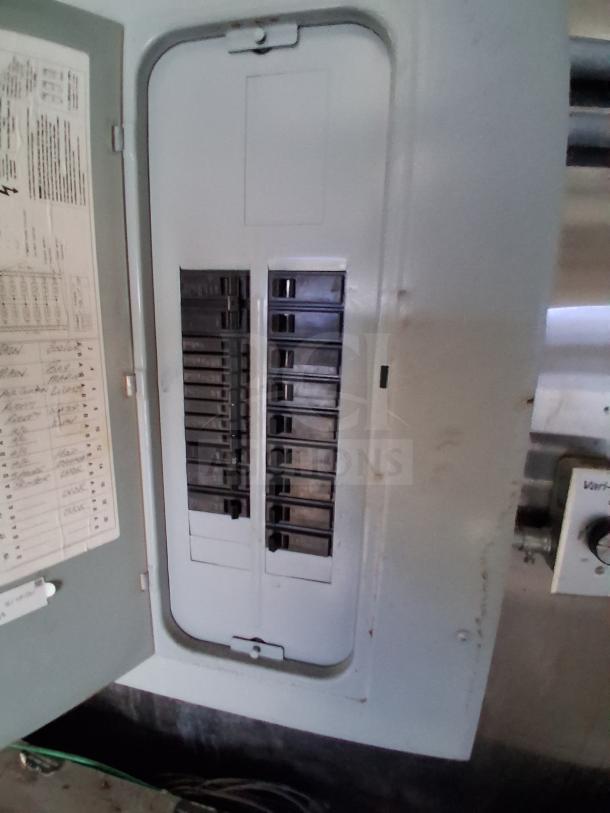 Electrical panel inside a mobile kitchen trailer, showing circuit breakers and labels, ensuring efficient power distribution.