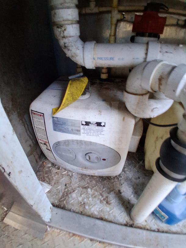 Alt text: Interior of a mobile kitchen trailer, showing plumbing connections and a water heater with labels.