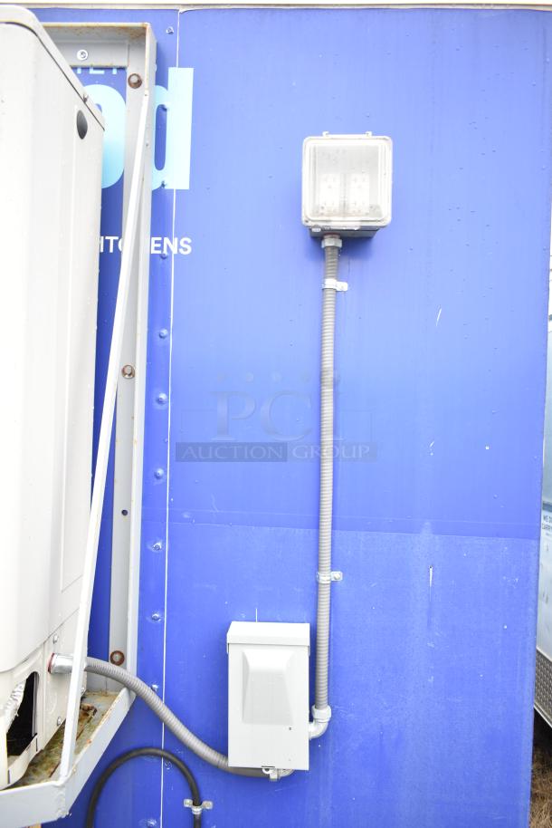 Blue exterior of a mobile kitchen trailer with visible electrical connections. Notable features include durable construction and ventilation system installation.