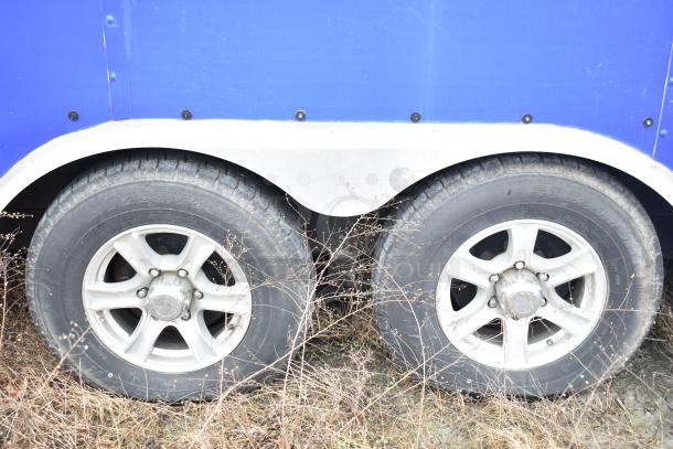 Dual axles of a blue commercial mobile kitchen trailer, equipped with sturdy tires for transport.